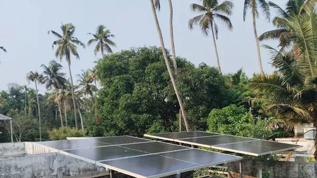Four solar panels on a low galvanised frame on a flat concrete roof, with the walkway along the parapet left clear.