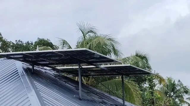 Solar panels on a trapezoidal sheet roof in Karukutty, Ernakulam, raised clear of the ridge on a galvanised mounting frame.