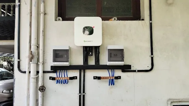 A rooftop solar inverter mounted on a wall beside its AC and DC isolators and the earth bar.